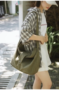Detail view of large olive canvas crossbody bag with silver button on a sunlit model