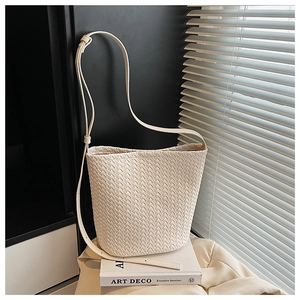 Detail of off-white woven bucket bag with adjustable strap on minimalist background