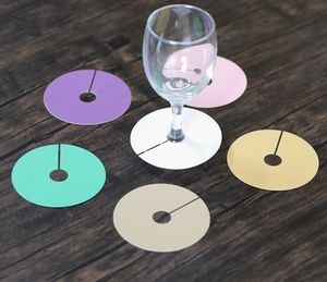 Détail de six marque-verres colorés pour verres à vin sur une surface en bois sombre