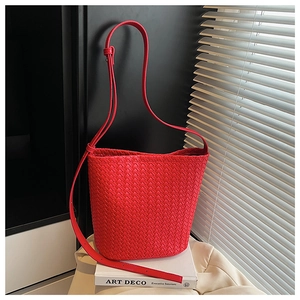Detailed view of red woven bucket bag with leather strap on a minimalist interior setting