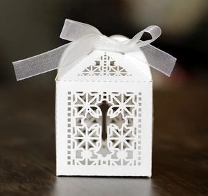 Close-up of white laser-cut candy box with cross pattern and ribbon bow for wedding