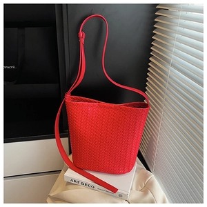 Detail shot of a red woven leather bucket bag leaning against white art books