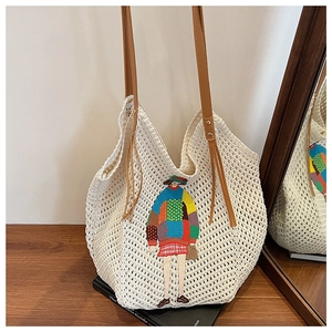 Close-up of cream knit tote bag with colorful embroidery and brown strap on a table