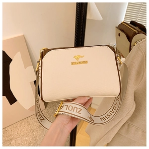 Detail of lychee textured leather bag with beige body and brown trim with wide canvas strap