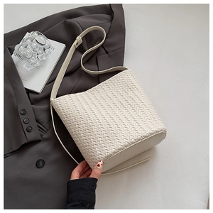 Close-up of cream woven bucket bag with detailed texture and matching shoulder strap
