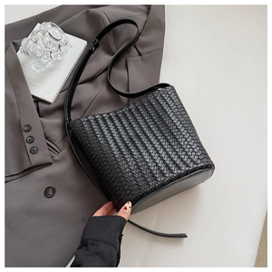 Detail of black woven leather bucket bag with slim shoulder strap in a minimalist setting