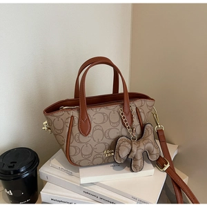 Detail einer Vintage-Monogramm-Handtasche mit Lederbesatz und Hundeanhänger auf Büchern