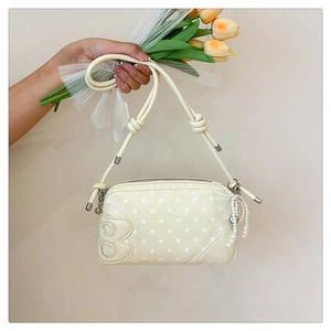 Detail of beige polka dot shoulder bag featuring pearl bow and metallic B charm decoration