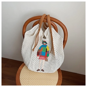 Close-up of crochet tote bag featuring artistic cartoon girl embroidery and leather tassels