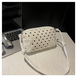 Close-up of white polka dot shoulder bag with B-letter patch and knotted strap detail