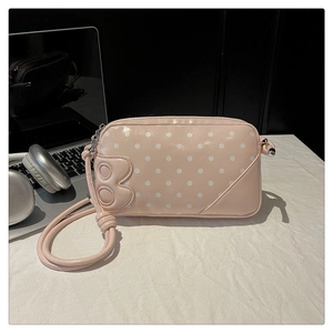 Detail of pink polka dot handbag with letter B emblem on white textured background