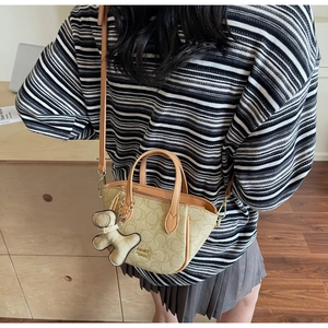 Detail der beigen Mini-Handtasche mit ovalem Muster, braunen Griffen und Bären-Anhänger