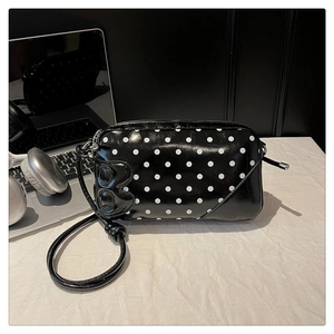 Close-up of black polka dot shoulder bag with glossy finish and bow charm detail
