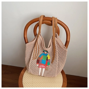 Detail of beige knitted tote bag featuring a cartoon embroidery and brown leather handles