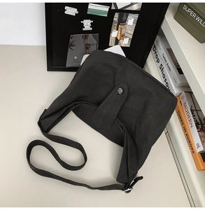 Detail of dark grey canvas crossbody bag showing metal snap button and soft fabric texture