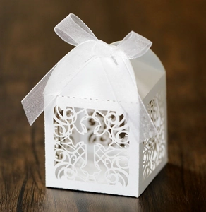 Detail of white laser-cut gift box with hollow cross and dove, featuring a silk bow