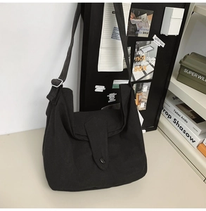 Detail shot of black canvas crossbody bag with flap cover on a minimalist wooden table