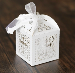 Detail of laser-cut flower patterns on a white candy box with ribbon and cross tag