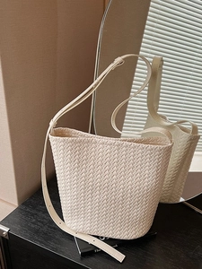 Elegant cream woven bucket bag with adjustable shoulder strap on a book base