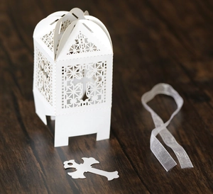 White laser-cut cross gift box with ribbon and pendant on a rustic wood background