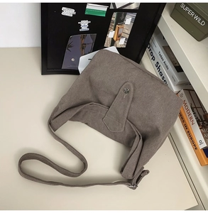 Brown canvas crossbody bag with silver buckle flap on a minimalist white table