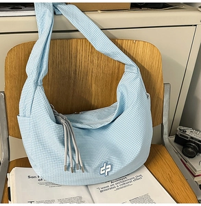 Close-up of light blue checkered hobo bag with logo embroidery and tassel on wood chair