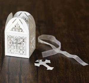 Close-up of white laser-cut wedding favor box with cross pattern and silk ribbon