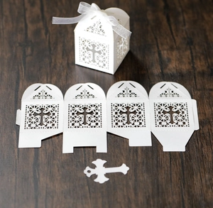 Detailed laser-cut white favor box with cross design and satin ribbon on wood surface