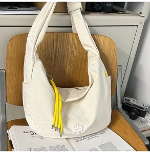 Detail of off-white checkered hobo bag with yellow woven pendant and embroidery on a chair