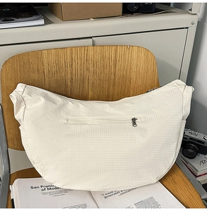 Detail of creamy white crescent bag with plaid texture and metal zipper on wooden chair
