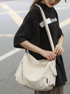 Grand sac cabas minimaliste en toile beige à bandoulière porté par un mannequin en extérieur