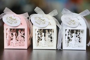Three elegant laser-cut wedding favor boxes with satin ribbons and golden thank you tags