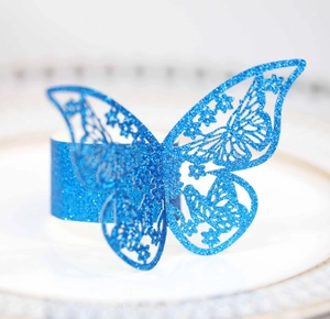 Vista macro de servilletero mariposa azul con purpurina y calados florales sobre un plato