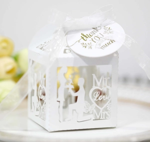 Detail of white hollow laser-cut wedding favor box with ribbon and thank you tag