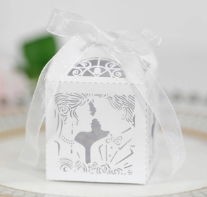 Detalle caja de dulces marfil cortada con láser con silueta de novios y cinta blanca