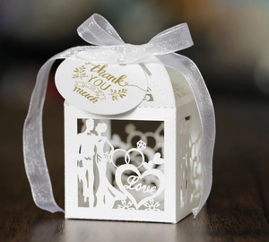 Macro shot of white laser-cut wedding candy box with heart ring design and thank you tag