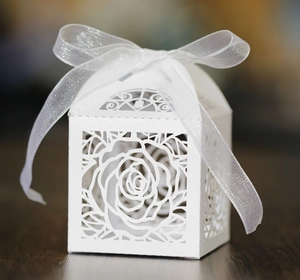 Macro detail of laser-cut white wedding favor box with rose patterns and organza ribbon bow