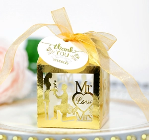 Detail of gold laser-cut wedding favor box with romantic proposal silhouette and ribbon