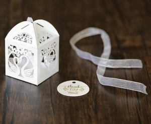 Detail of white laser-cut swan candy box with sheer ribbon and thank you gift tag