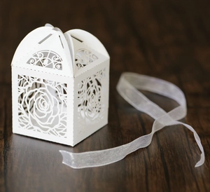Detailed laser-cut white wedding favor box with rose patterns and ribbon on wood