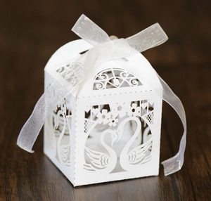 Detail of laser-cut swan hollow paper candy box with white organza ribbon on wood
