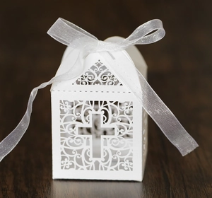 Detail of laser cut cross candy box with white ribbon on dark wood surface
