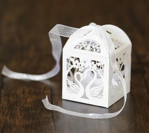 Macro shot of white laser-cut swan hollow candy box with elegant white ribbon detail