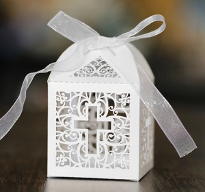 Close-up of laser-cut hollow cross design on white wedding favor box with ribbon