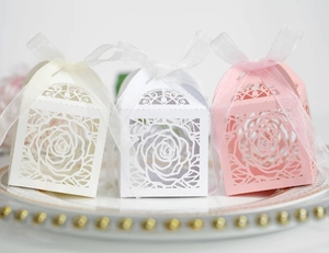 Laser-cut wedding favor boxes with rose patterns and matching organza ribbons on a plate