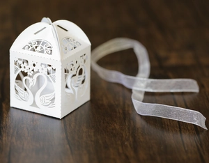 Detail of white laser-cut swan candy box with intricate floral patterns and ribbon