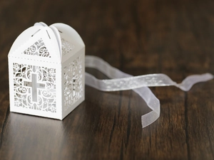 Detailed laser-cut white favor box with cross pattern and white ribbon on wood