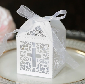 Close-up of white laser-cut cross candy box with ribbon bow on an elegant plate