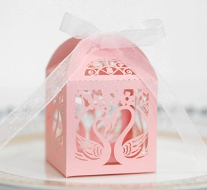 Laser-cut hollow swan wedding candy box in light pink with white sheer ribbon on porcelain
