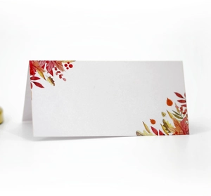 Macro detail of white folded place card with autumn maple leaves and red berry printing